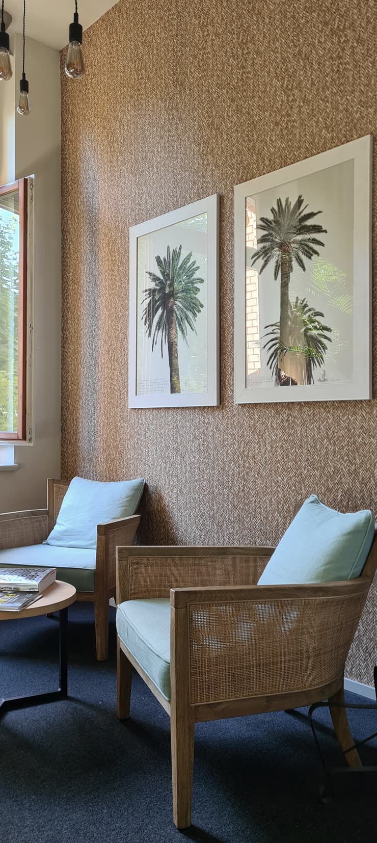 Armchairs beneath palm prints on a tall wallpapered wall