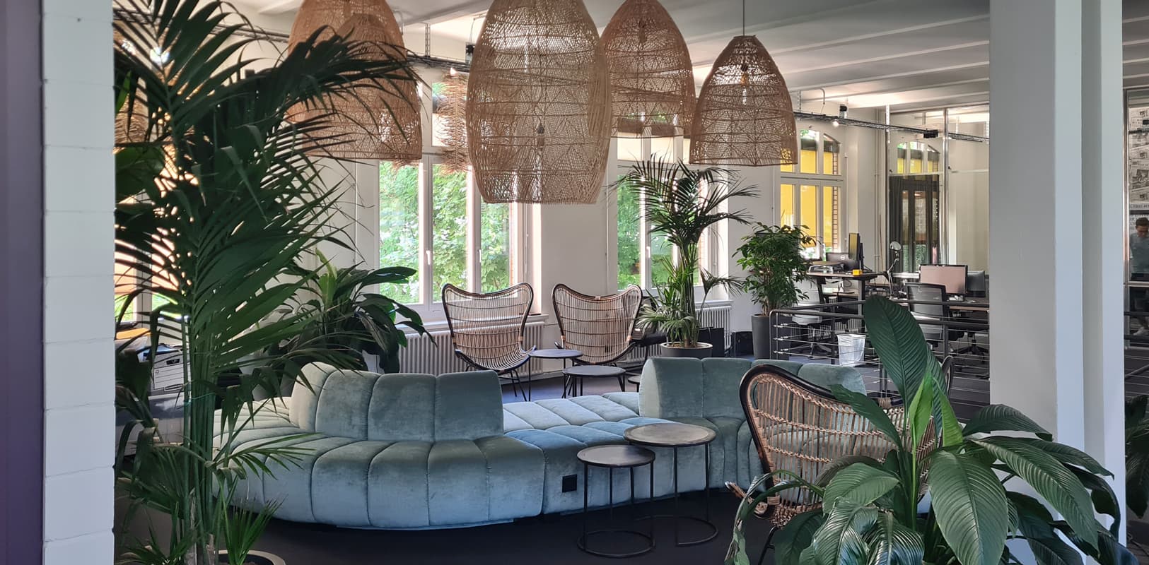 Open lounge with mint sofa, rattan pendant lights, and plants